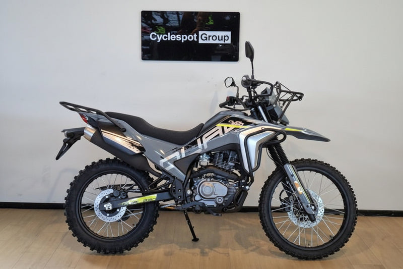 Load image into Gallery viewer, A silver and black 2026 CFMOTO CFLITE 230 Dual dual-sport motorcycle with yellow accents, parked indoors on a wooden floor against a white wall with a 'Cyclespot Group' sign above it.