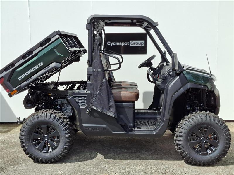 Load image into Gallery viewer, A green 2026 CFMOTO UFORCE U10 PRO side-by-side utility vehicle with its cargo bed raised, parked on a concrete surface against a light gray wall. The vehicle features a dark green and black tonneau cover, a black roll cage, and large off-road tires.