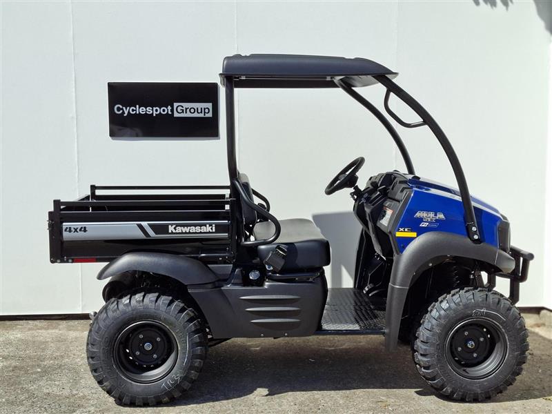 Load image into Gallery viewer, A 2017 Kawasaki Mule KAF 400 KH 4x4 utility vehicle with a black roll cage and cargo bed, parked outdoors against a white wall. The vehicle features a blue front hood and a black 'Cyclespot Group' sign mounted on the rear side.