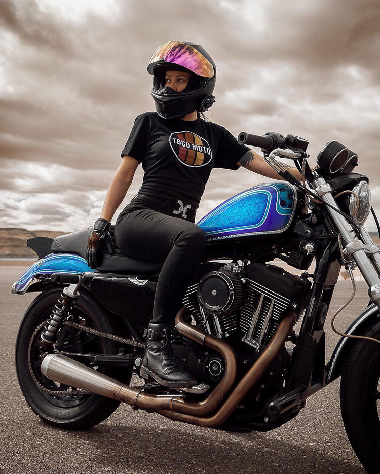 A female rider on a custom motorcycle wearing slim-fit protective women’s motorcycle pants. Stylish and tapered for urban riding. Available at Cyclespot Auckland, Taranaki, Wellington, and online nationwide.