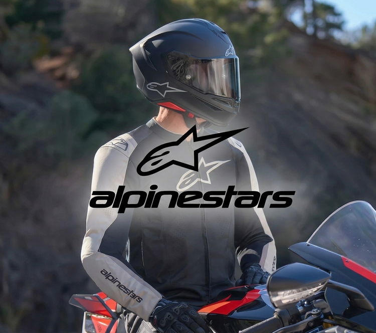 A close-up view of a motorcyclist wearing a black and white Alpinestars leather riding jacket with protective armor and a matching full-face helmet. He is sitting on a high-performance sportbike, with the brand's iconic logo clearly displayed on his gear.