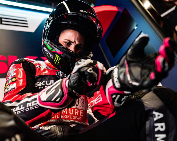 A professional female racer adjusting her Alpinestars Stella leather racing gloves with pink accents. High-performance women's motorcycle gear at Cyclespot Auckland, Taranaki, and Wellington.