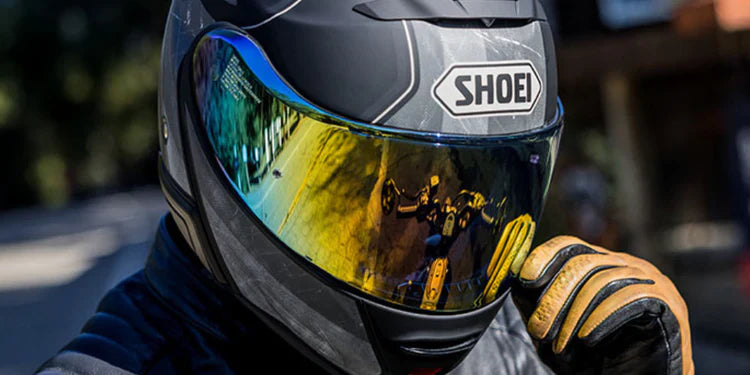 Close-up of a rider wearing a Shoei road helmet with a gold iridescent tinted visor and tan leather gloves. Premium Shoei helmets available for professional fitting at Cyclespot Auckland, Taranaki, and Wellington.