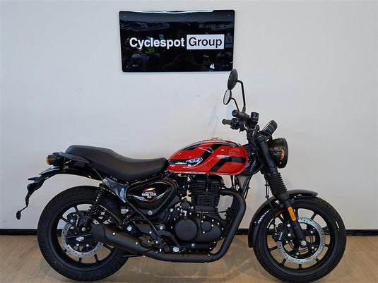 A red and black street motorcycle, identified as a Royal Enfield Hunter Premium, parked indoors against a white wall with a 'Cyclespot Group' sign above it.