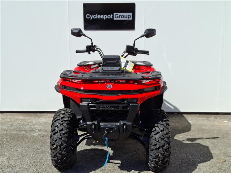 Load image into Gallery viewer, A red and black 2026 CFMOTO CFORCE C5 EPS ATV is photographed from the front, parked on asphalt in front of a white wall with a 'Cyclespot Group' sign above it.
