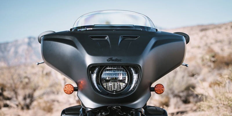 Load image into Gallery viewer, Front view of a 2026 Indian Chieftain Dark Horse motorcycle with a clear windshield and round headlight, set against a blurred desert landscape background.
