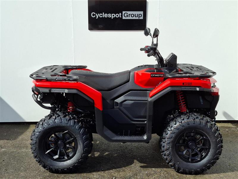 Load image into Gallery viewer, A red and black 2026 CFMOTO CFORCE C5 EPS quad bike with knobby tires, rear cargo racks, and side mirrors, parked in front of a white wall with a 'Cyclespot Group' sign.
