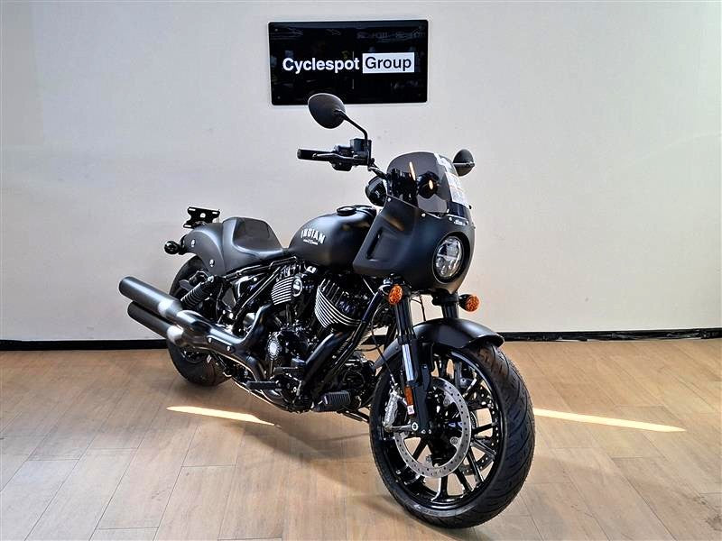 Load image into Gallery viewer, A black Indian Sport Chief motorcycle is parked indoors on a light wood floor against a white wall, with a 'Cyclespot Group' sign visible above it.
