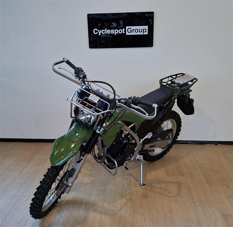 Load image into Gallery viewer, A green and black Stockman off-road motorcycle with a rear luggage rack, displayed on a wooden floor against a white wall with a 'Cyclespot Group' sign.
