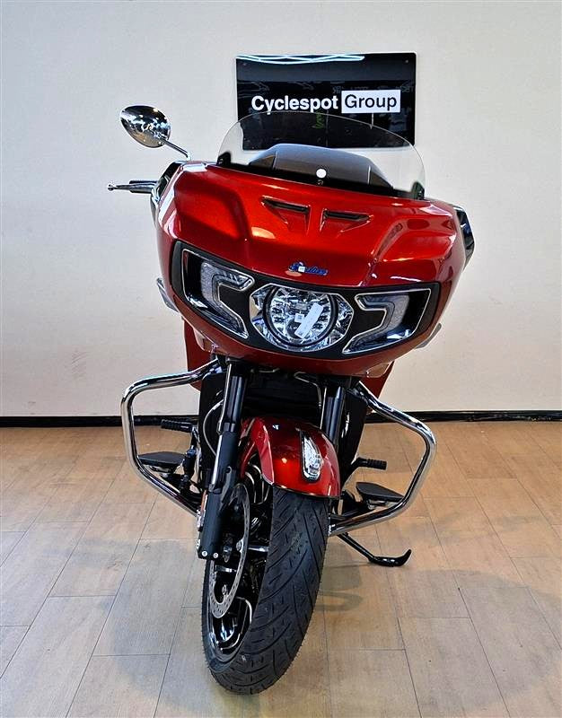 Load image into Gallery viewer, A red Indian Challenger Ltd motorcycle with a clear windshield and chrome crash bars, photographed indoors against a plain beige wall and light wood floor. A sign reading 'Cyclespot Group' is visible behind the windshield.

