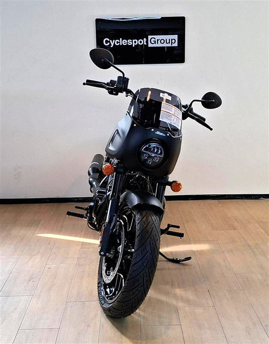 A black Indian Sport Chief cruiser motorcycle with a windscreen and orange turn signals, photographed indoors against a white wall with a 'Cyclespot Group' sign above it and light wood flooring.
