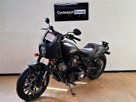 A black Indian Sport Chief motorcycle is parked indoors on a wooden floor against a light gray wall, with a 'Cyclespot Group' sign visible above it.