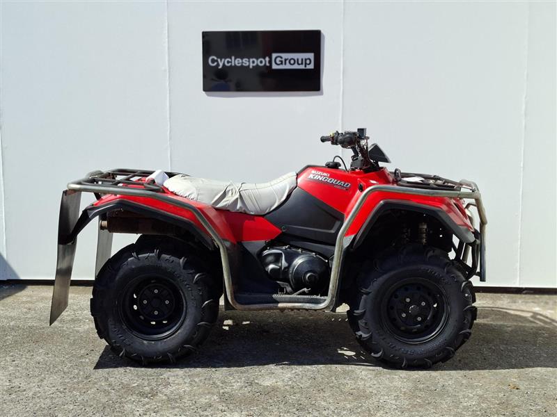 Load image into Gallery viewer, A red and black 2024 Suzuki King Quad LT-A400F ATV with a white seat cover, parked in front of a white wall with a 'Cyclespot Group' sign.
