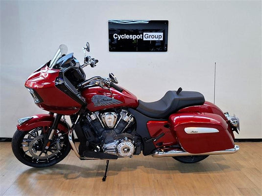 A red and black Indian Challenger motorcycle is parked indoors on a wooden floor against a light gray wall, with a 'Cyclespot Group' sign visible on the wall behind it.
