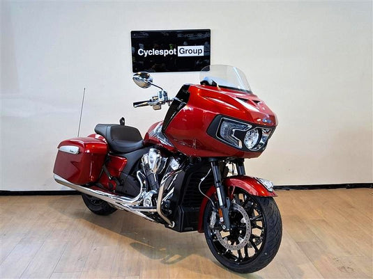 A red Indian Challenger Ltd touring motorcycle with chrome exhausts and a clear windshield, photographed indoors against a light wall with a visible Cyclespot Group sign.