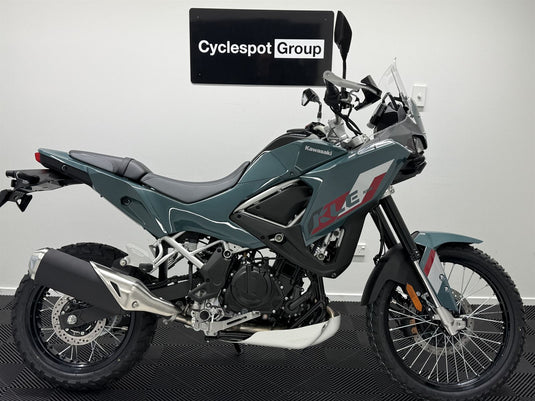 A Kawasaki KLE adventure-touring motorcycle in a dark teal-gray color, photographed from the side against a light gray wall with a 'Cyclespot Group' sign in the background.