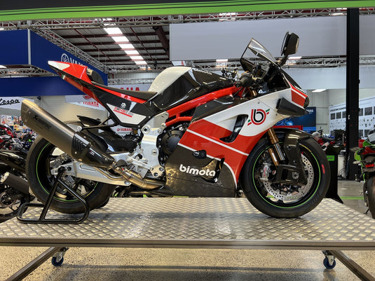 A red, white, and black Bimoto sport motorcycle displayed on a metal platform inside a showroom or exhibition hall.