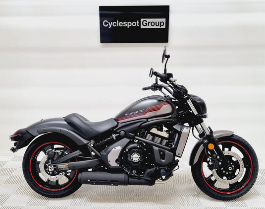 A black and dark gray Kawasaki Vulcan cruiser motorcycle with red accents on the wheels, displayed in a showroom with a 'Cyclespot Group' sign on the wall behind it.