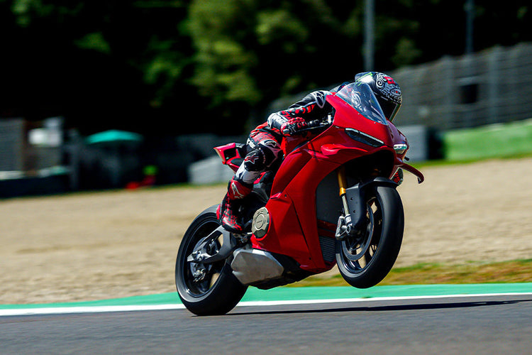 Rider in Alpinestars racing leathers performing a wheelie on a red Ducati Panigale V4 at the track. Shop the look at Cyclespot NZ.