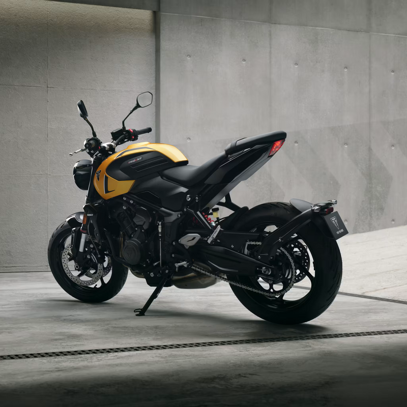 Load image into Gallery viewer, A black and yellow 2026 Triumph Trident 660 LAMS motorcycle parked on a concrete surface against a textured gray concrete wall.
