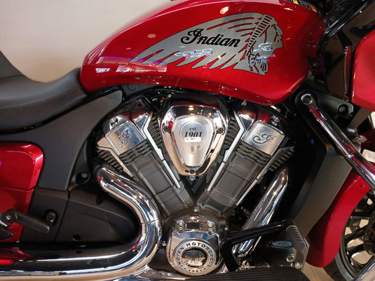 Close-up of a red Indian motorcycle showing the fuel tank decal, chrome V-twin engine, exhaust pipes, and part of the black seat.