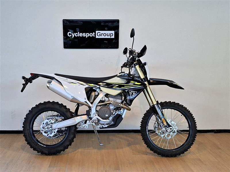 Load image into Gallery viewer, A Triumph TF 250 E dirt bike with a black, white, and yellow color scheme, displayed on a wooden floor against a white wall with a 'Cyclespot Group' sign.
