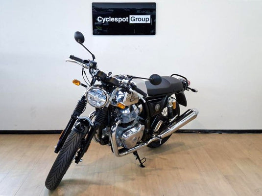 A black and silver 2026 Royal Enfield Continental GT Classic motorcycle is parked indoors on a light wood floor against a white wall, with a 'Cyclespot Group' sign visible above it.