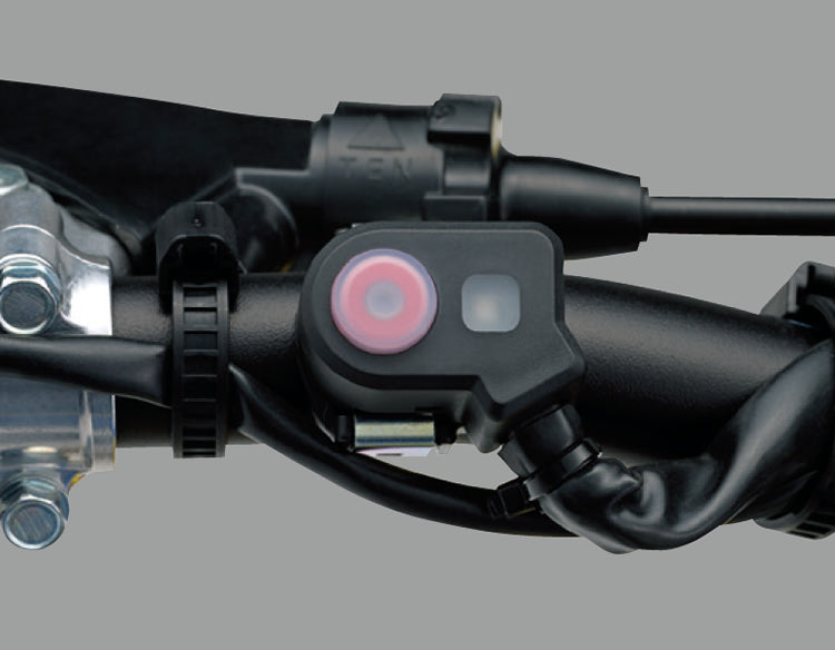 Load image into Gallery viewer, A close-up of a black handlebar-mounted electronic holeshot device with a pink circular button and a small square light, attached to a motorcycle handlebar assembly against a plain gray background.
