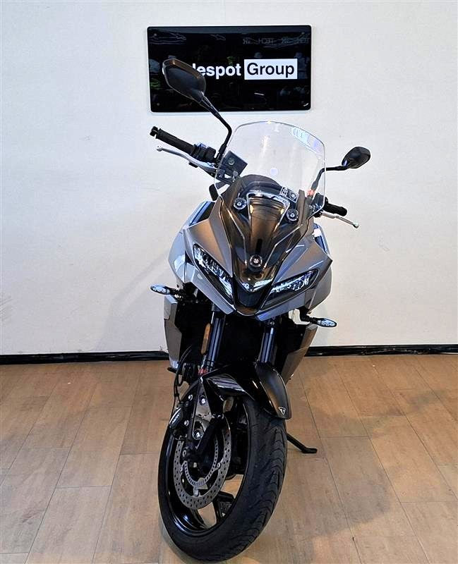 Load image into Gallery viewer, A grey  2023 Triumph Tiger Sport 660  motorcycle is parked indoors on a wooden floor against a white wall, with a 'spot Group' sign visible above it.
