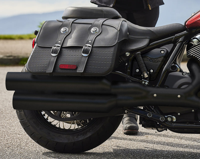 Load image into Gallery viewer, A close-up side view of a black leather motorcycle saddlebag bag mounted on the rear of an Indian Super Chief cruiser motorcycle, with a person's leg visible standing beside it on an outdoor paved surface.
