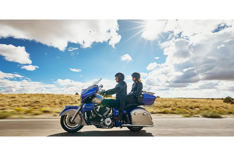 Load image into Gallery viewer, A blue and silver Roadmaster touring motorcycle with two riders traveling on a paved road under a bright blue sky with sun rays and clouds.
