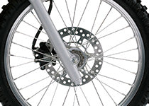 Close-up of a motorcycle or dirt bike front wheel featuring a silver metallic disc brake, multi-spoke wheel, and part of the tire.
