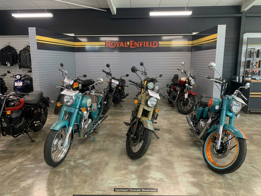 Interior of Cyclespot Taranaki featuring the modern Royal Enfield showroom. High-definition view shows six classic motorcycles, including teal, olive, and red models, and the 'ROYAL ENFIELD' wall logo.